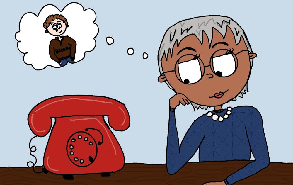 A cartoon of an older woman sitting by a red telephone, with a cartoon thought bubble stemming from her head containing a picture of a boy in a Brown sweatshirt.