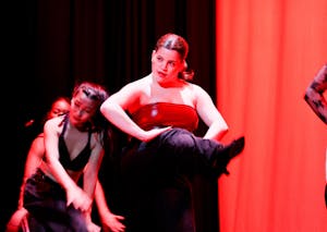 A dancer wearing a red top with her foot kicked out and looking out at the audience. 