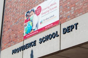 A photo of the Providence School Department building, with the words "Providence School Dept" on the building. On the building's brick wall there is a poster advertising the Providence Schools Early Childhood Program.