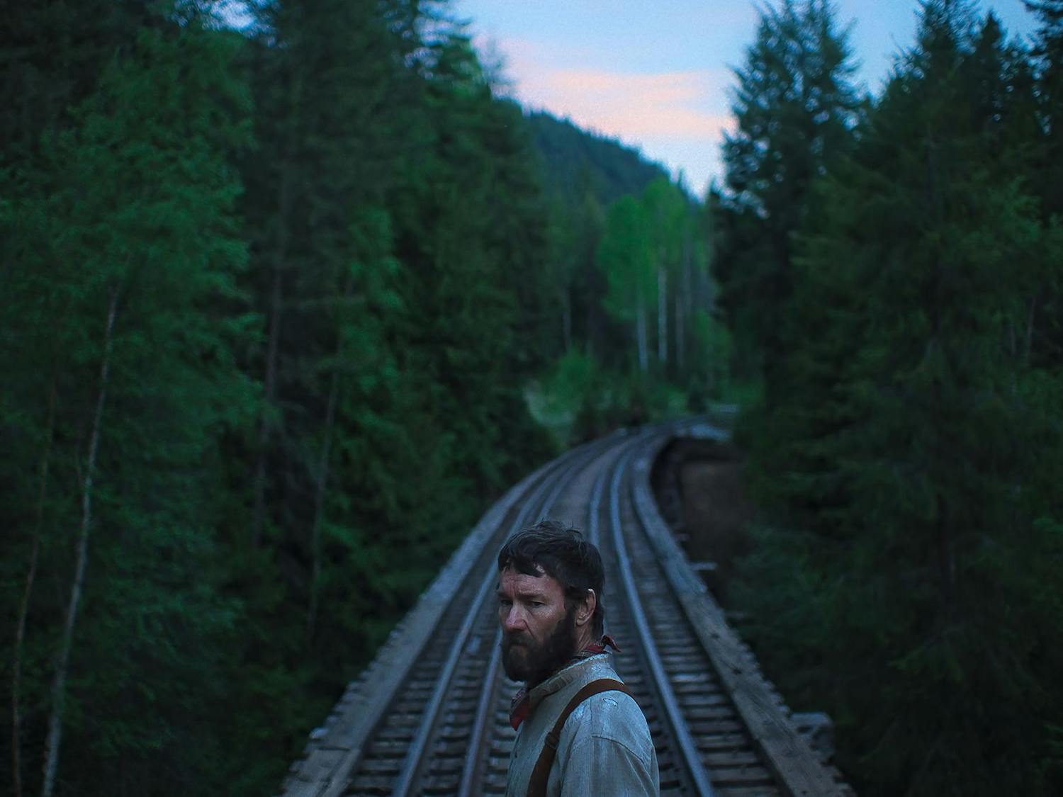 A photo shows Joel Edgerton as Robert Grainier, a bearded logger framed in the center of train tracks surrounded by trees.