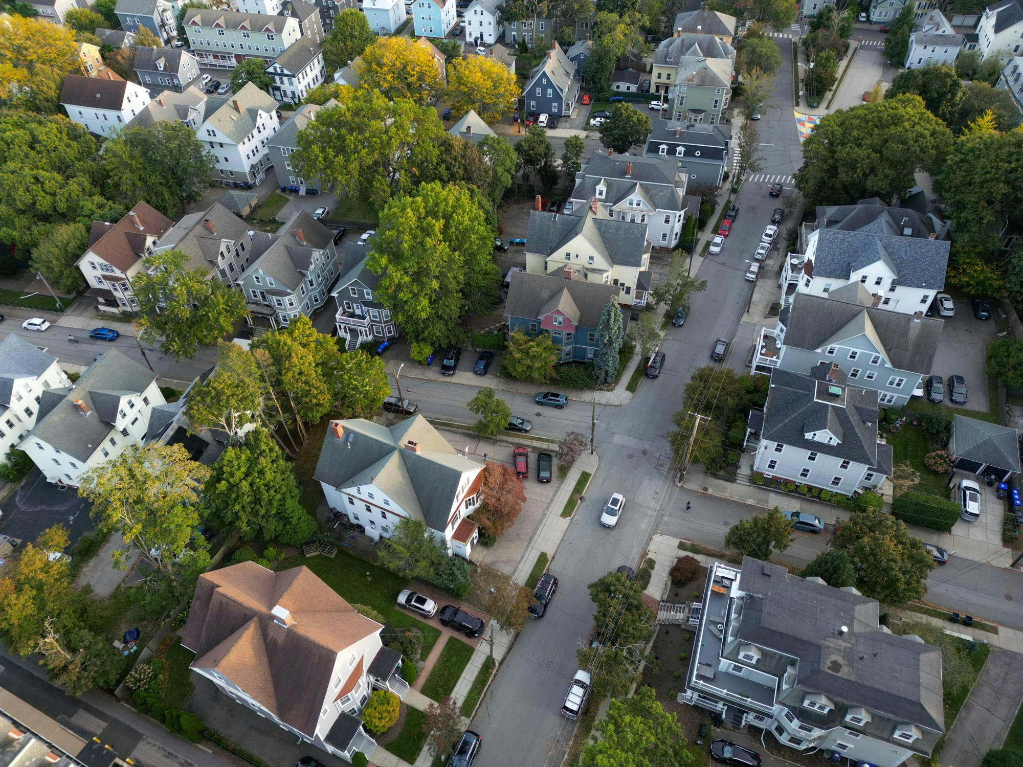 A drone shot of several houses during the day with multiple cars driving down the streets.