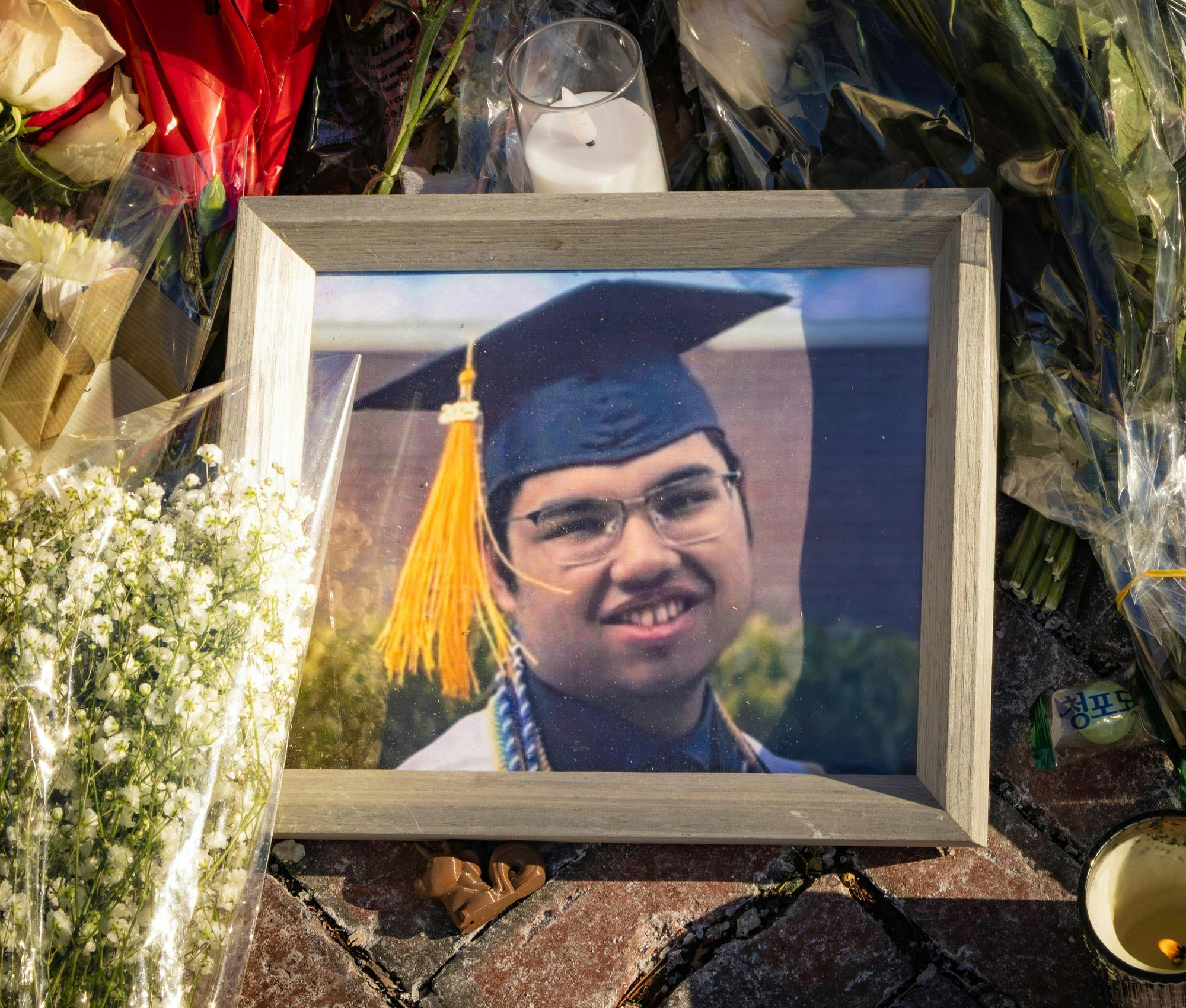 A picture frame containing a photo of Mukhammad Aziz Umurzokov wearing a blue graduation cap. The frame is surrounded by flowers. 