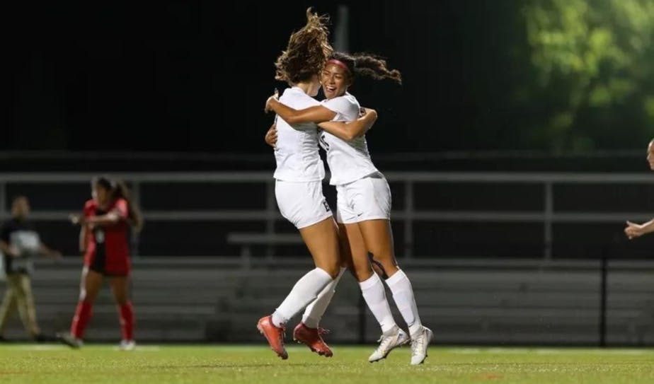 A photo of two Brown players, both wearing white jerseys, hugging on the soccer field.