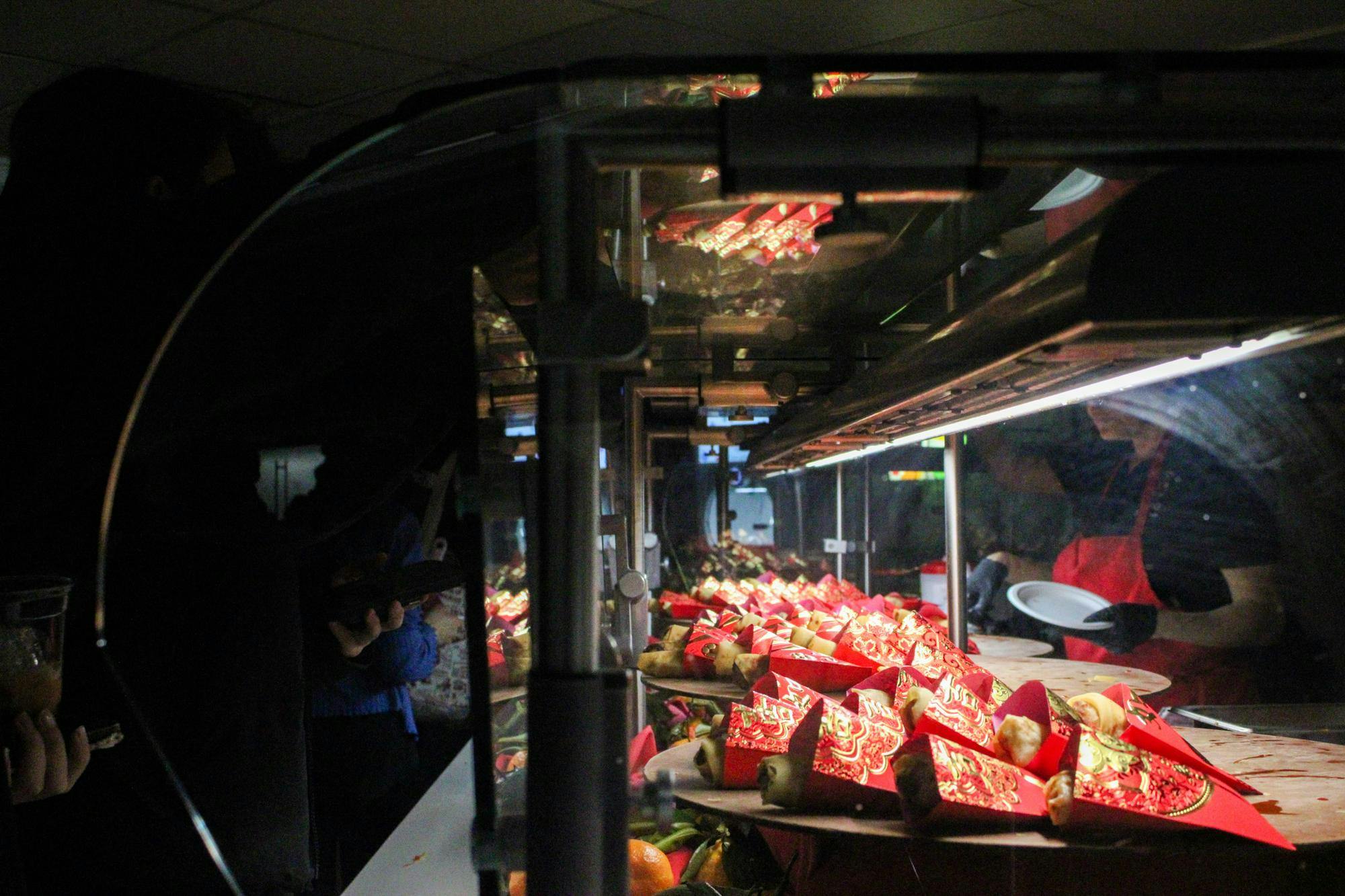 Photo of spring rolls in a glass case individually wrapped in red envelopes served on round brown plates.