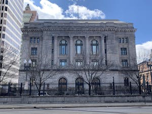 The United States District Court for the District of Rhode Island building with a fence, trees and a road in the foreground. 