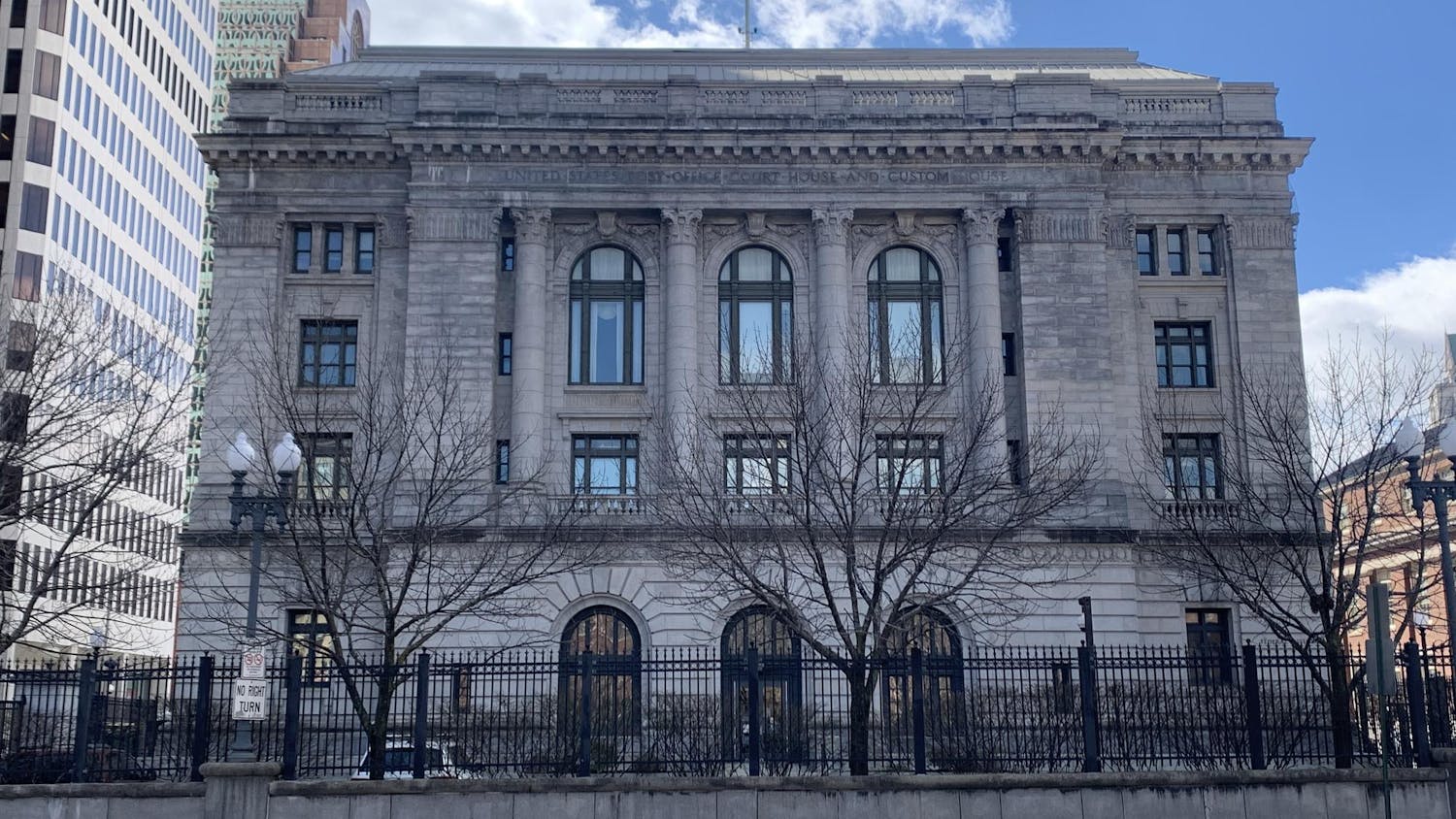 The United States District Court for the District of Rhode Island building with a fence, trees and a road in the foreground.