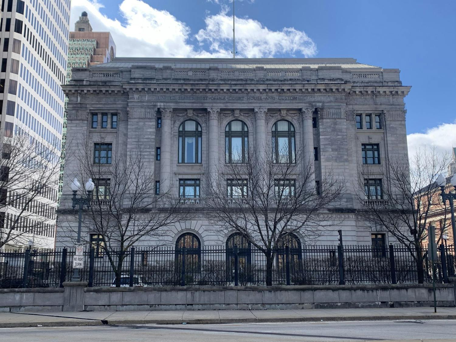 The United States District Court for the District of Rhode Island building with a fence, trees and a road in the foreground.