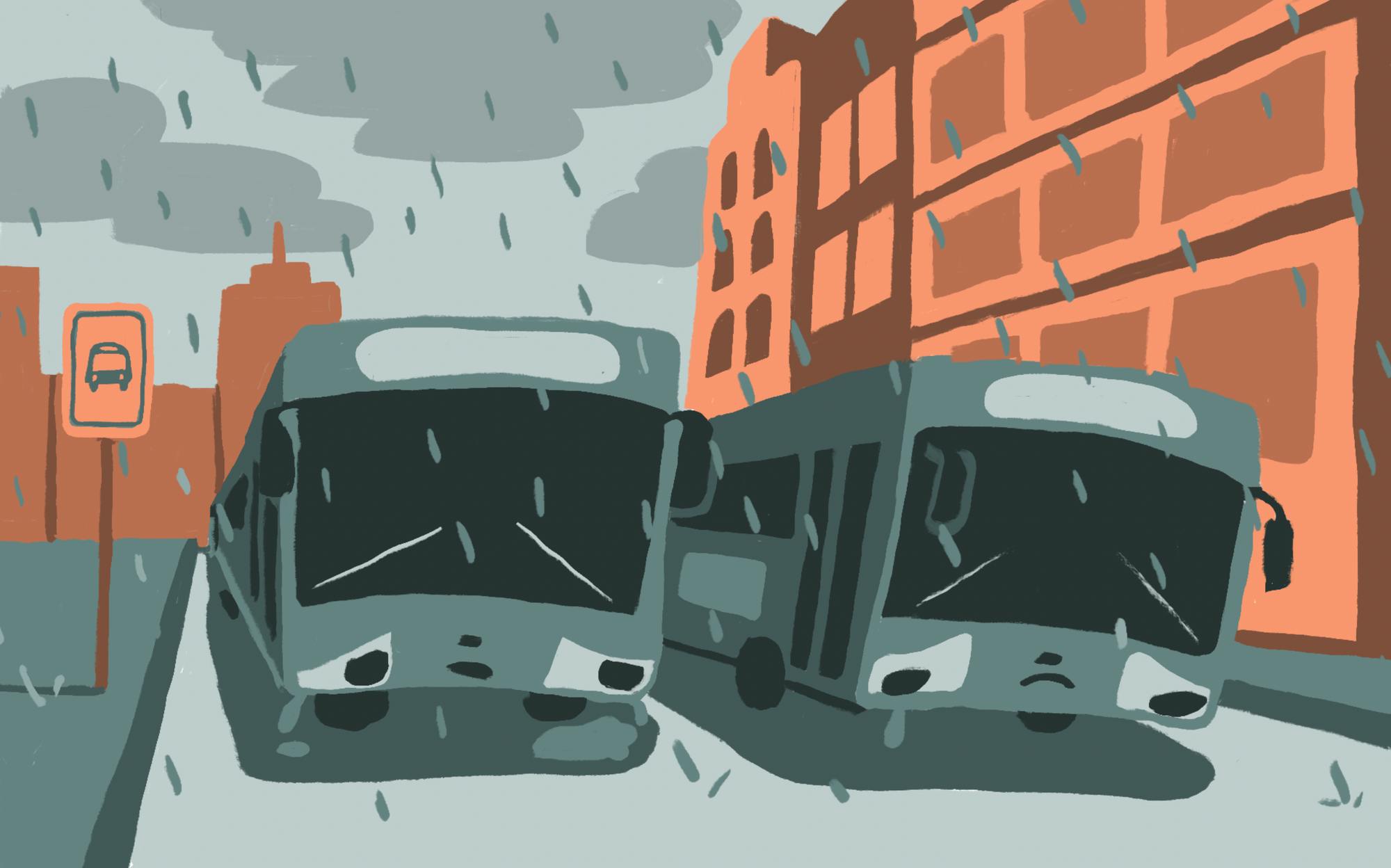 Two gray busses sit in the rain surrounded by orange buildings. 