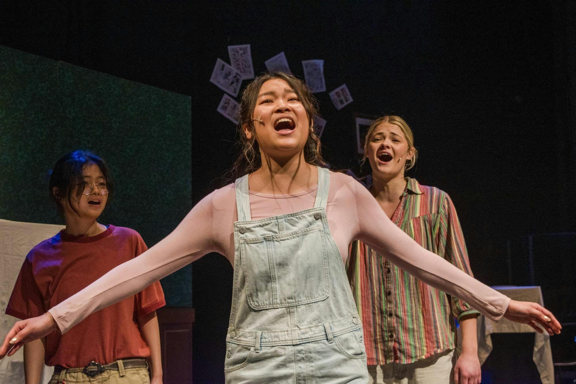 A photo of Nina Sethanandha ’29, playing Small Alison, in the center with her arms outstretched. Jocelyne Lioe ’29, playing present-day Allison is to her left, and Dylan George ’29, playing Medium Alison, is to her right.