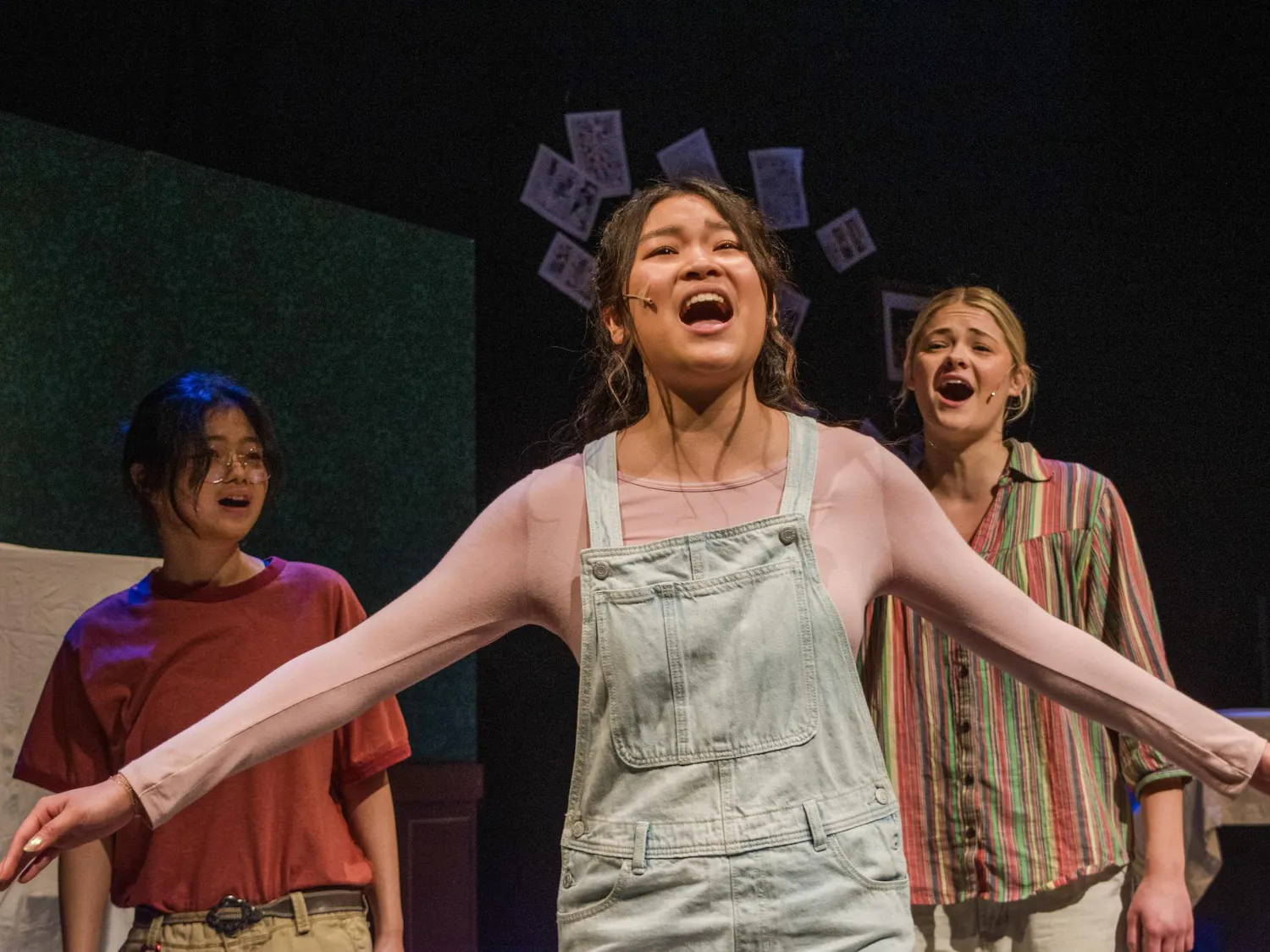 A photo of Nina Sethanandha ’29, playing Small Alison, in the center with her arms outstretched. Jocelyne Lioe ’29, playing present-day Allison is to her left, and Dylan George ’29, playing Medium Alison, is to her right.