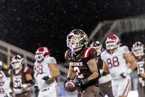 A photo of a Brown football player holding a football and yelling in celebration. Behind him are players from both teams. 