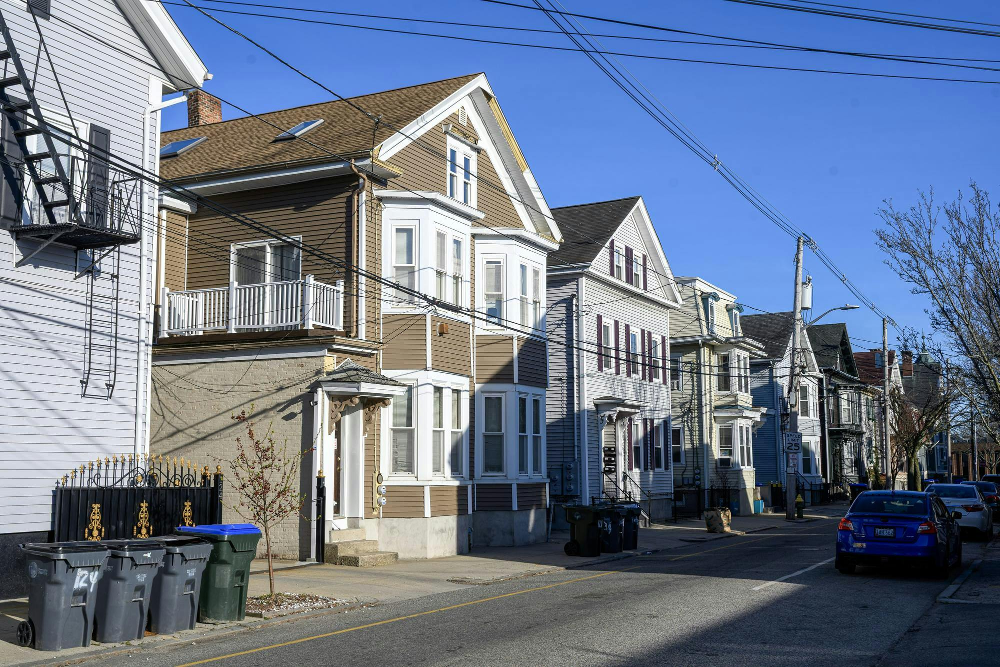 A photo of a street with multiple houses on the right side and cars on the left side.