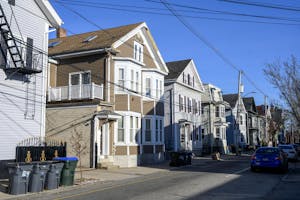 A photo of a street with multiple houses on the right side and cars on the left side.