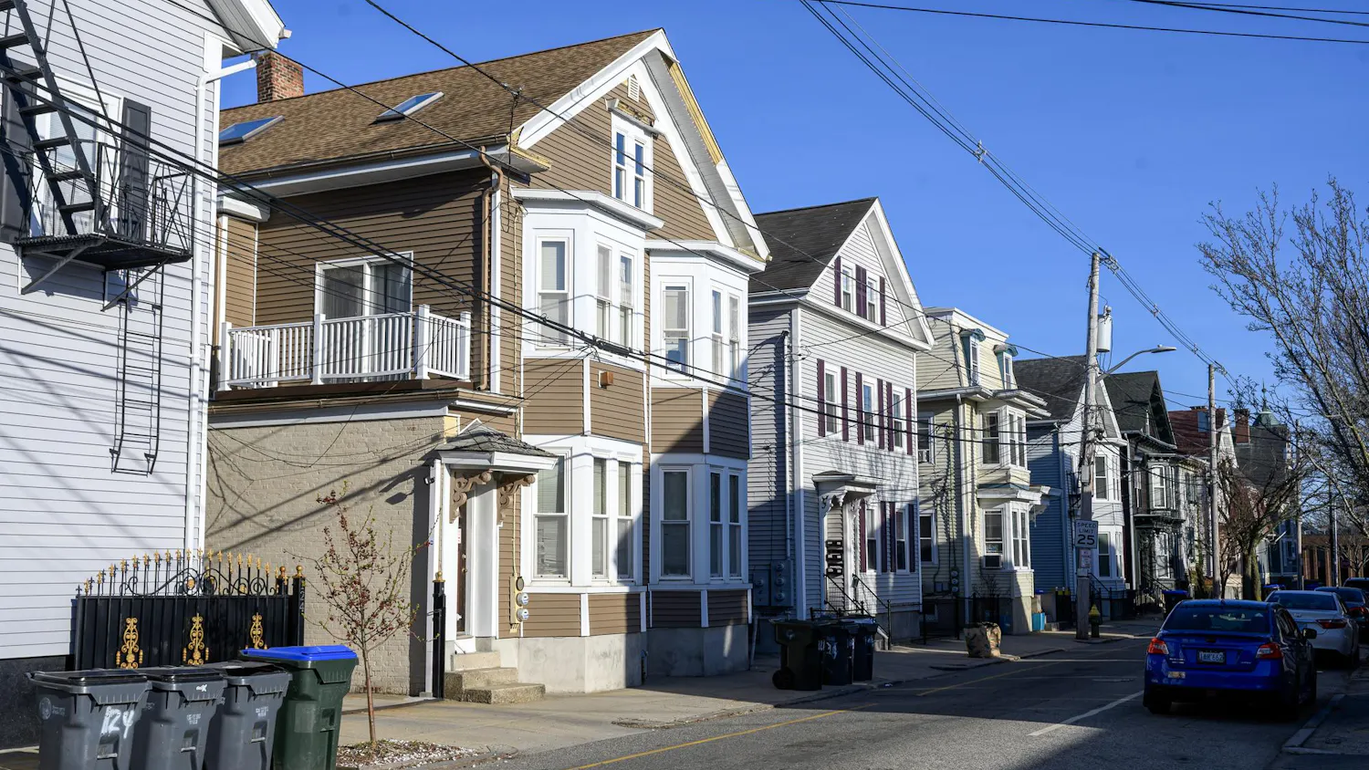 A photo of a street with multiple houses on the right side and cars on the left side.