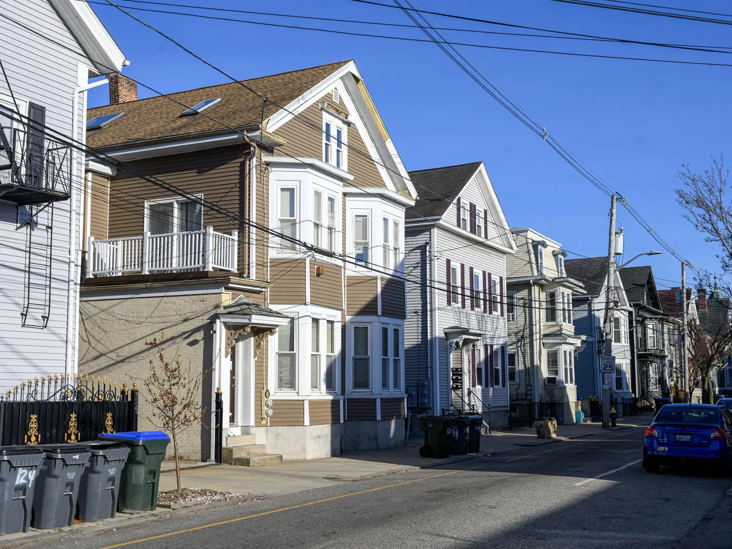 A photo of a street with multiple houses on the right side and cars on the left side.
