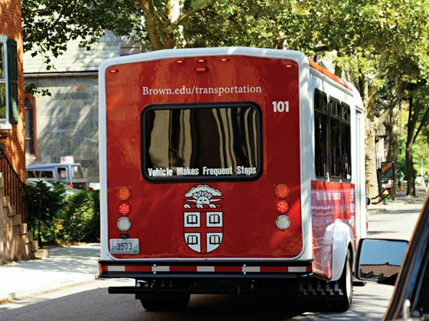 A Brown bus drives away down George St. on a summer day.