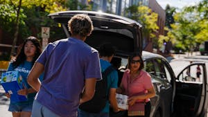 A boy in a purple shirt faces away from the camera as two move-in helpers and a parent carry drinks.