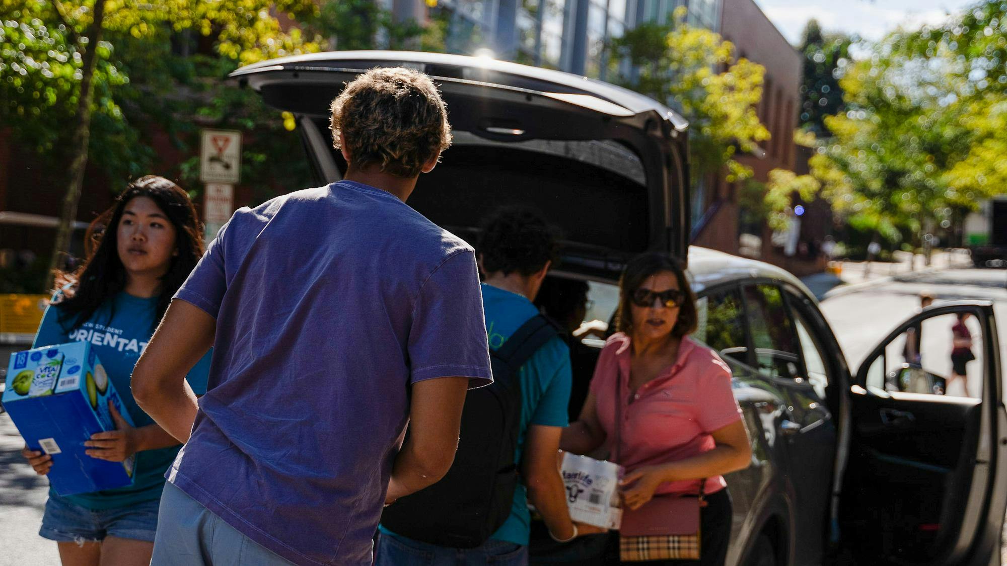 A boy in a purple shirt faces away from the camera as two move-in helpers and a parent carry drinks.