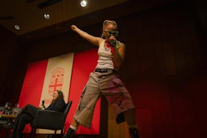 JoJo Siwa performs on stage at Salomon DECI at Brown University in a white tank-top and cargo jeans with a Brown University crest in the background.