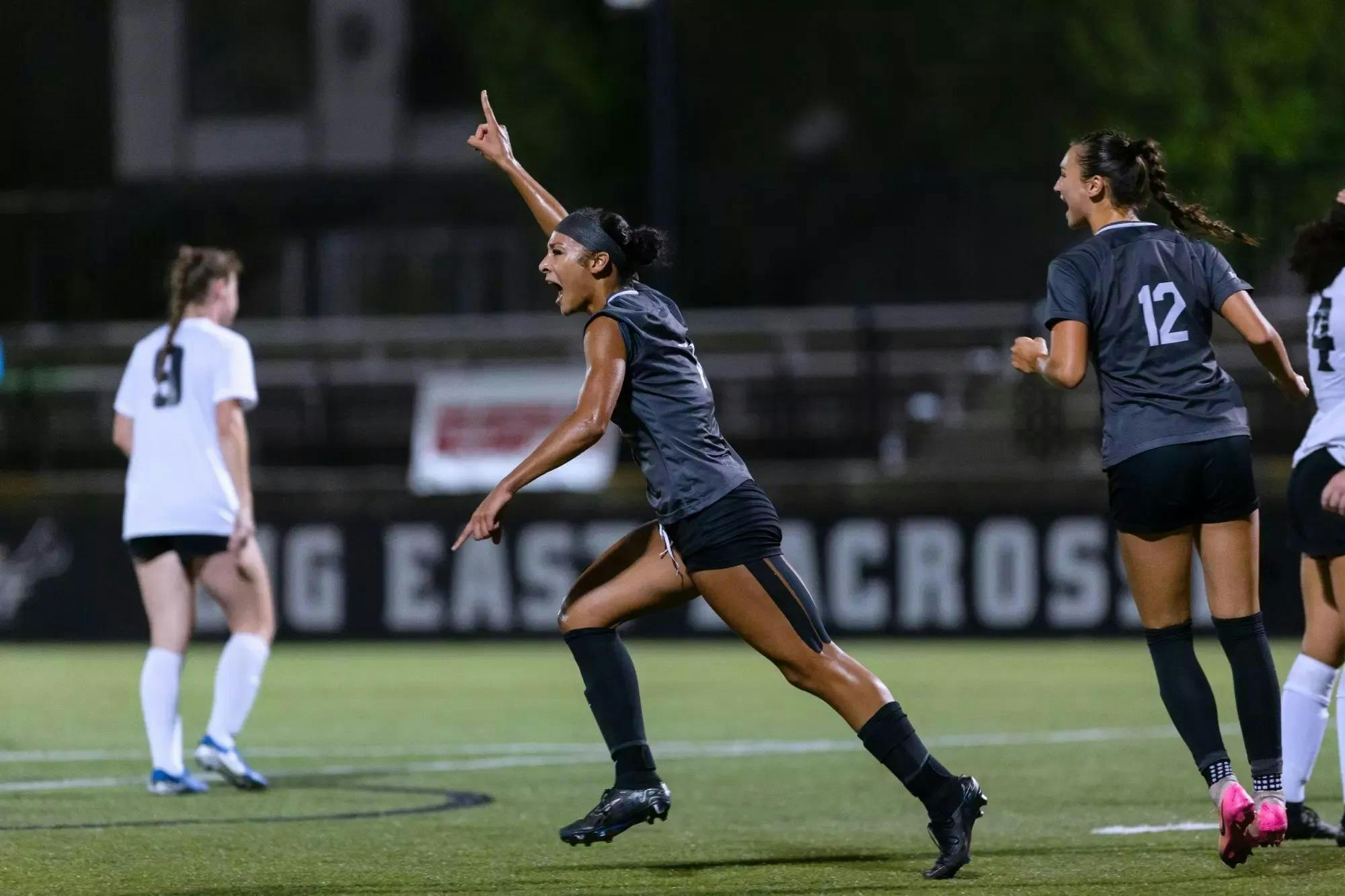 Photo of a soccer player running on the field with one finger pointing towards the sky.