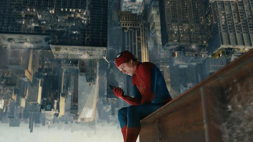 A photo of Spiderman, played by Tom Holland, sitting on a large support beam looking at his phone with his mask on top of his head. The upside down skyline of New York City is in the background.