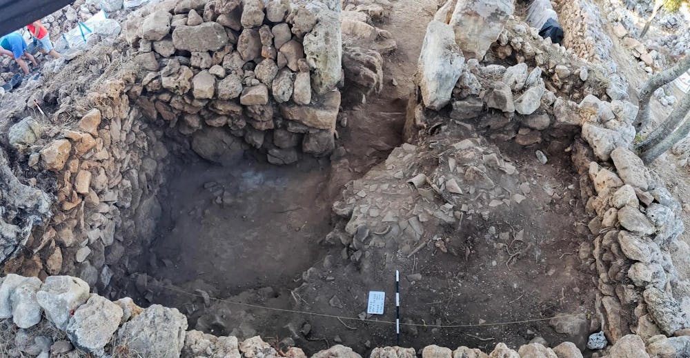Photo of the archeological site, with rocks surrounding the cleared-out space. 