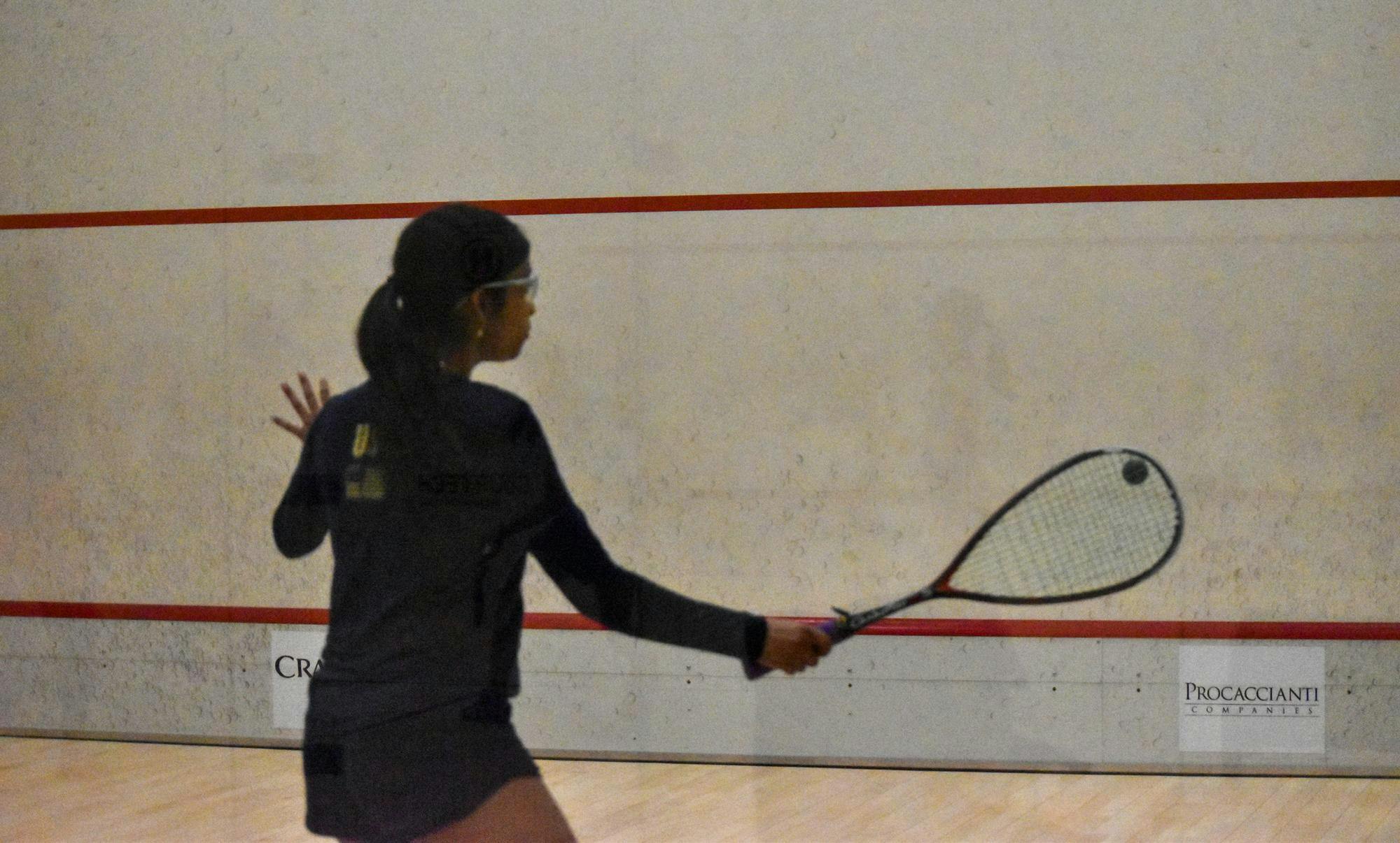 Photo of a member of the Brown Squash team wearing all navy hitting a ball at a wall with a racket during practice. 