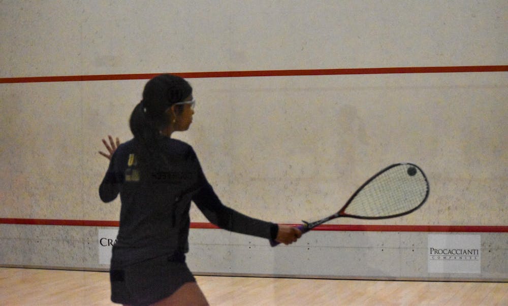 Photo of a member of the Brown Squash team wearing all navy hitting a ball at a wall with a racket during practice. 