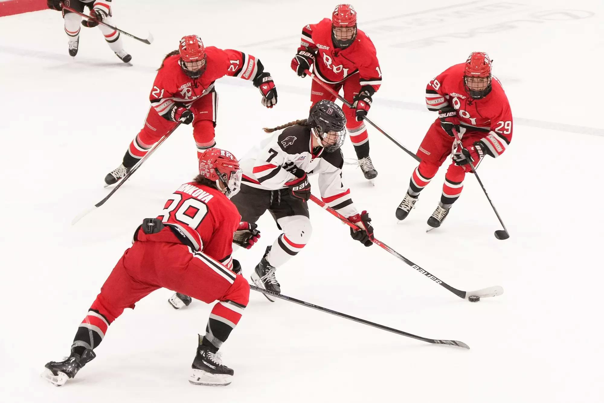 An aerial view of three RPI women's hockey players in red uniforms surrounding a Brown women's hockey player in a white uniform.