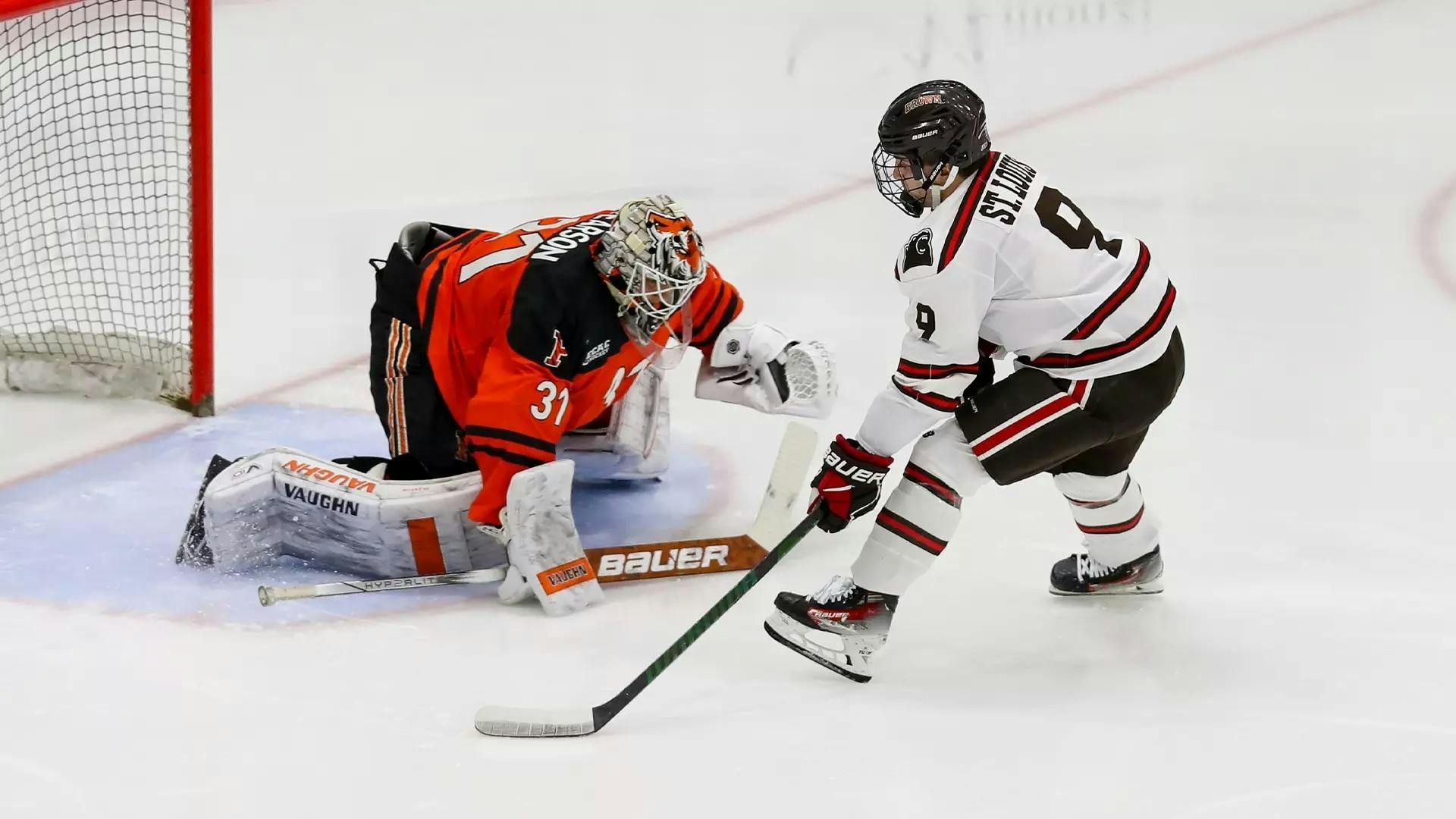 Two men play hockey on an ice rink, Brown player tries to make a goal while Princeton player tries to stop him.