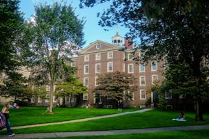 University Hall on a bright day surrounded by trees with multiple students scattered on the green in the front.