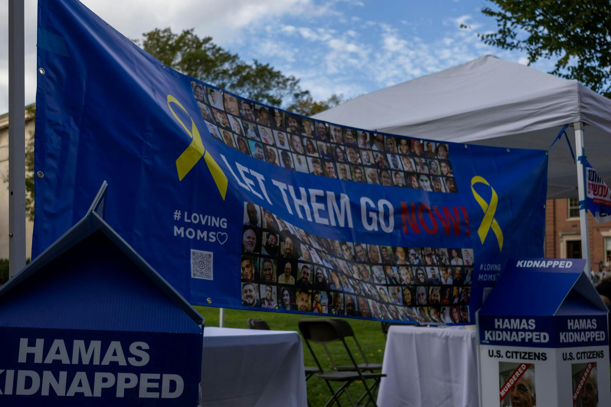 Photo of Brown-RISD Hillel's October 7th display, which shows a banner that reads "Let them go now!" and large blue milk cartons with missing people's faces on them.