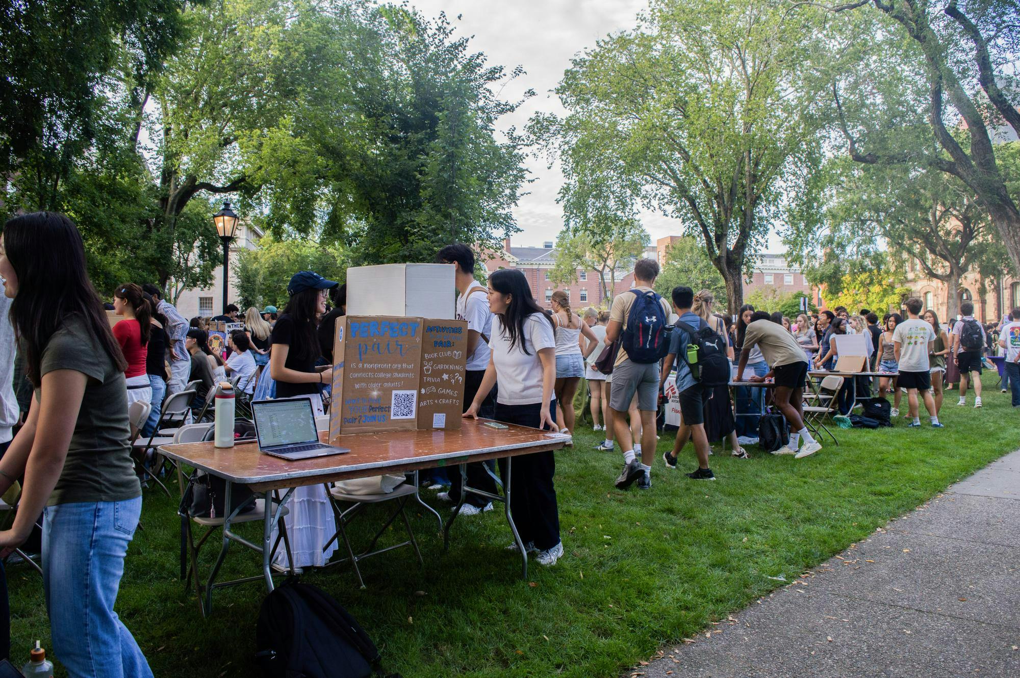 A photo showing people walking around the Main Green visiting tables lined up in rows and topped with poster boards of different student clubs. 