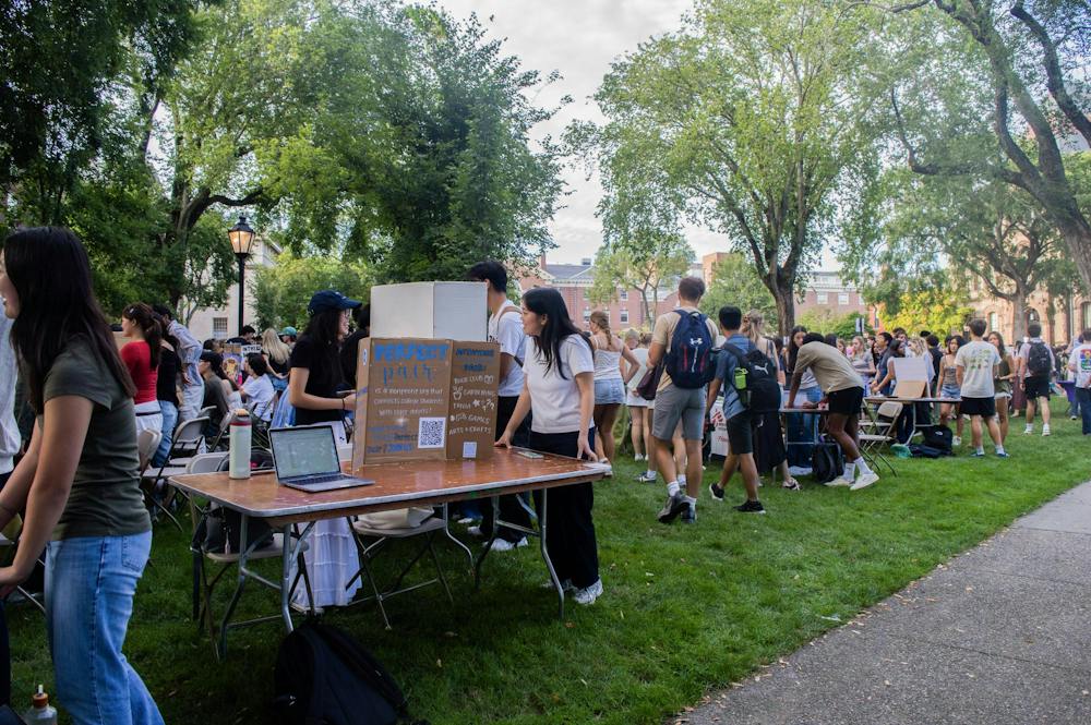 A photo showing people walking around the Main Green visiting tables lined up in rows and topped with poster boards of different student clubs. 
