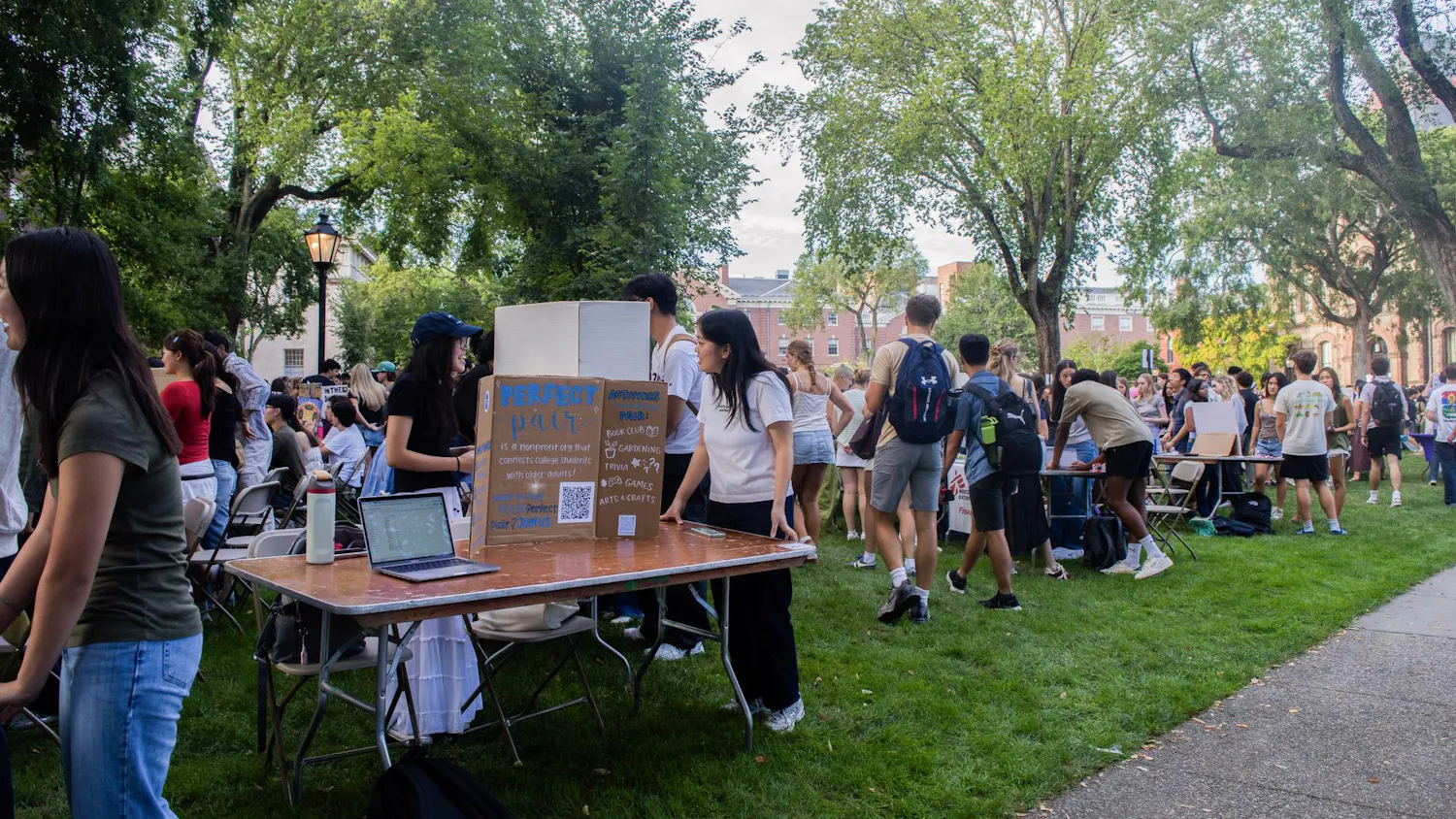 A photo showing people walking around the Main Green visiting tables lined up in rows and topped with poster boards of different student clubs.