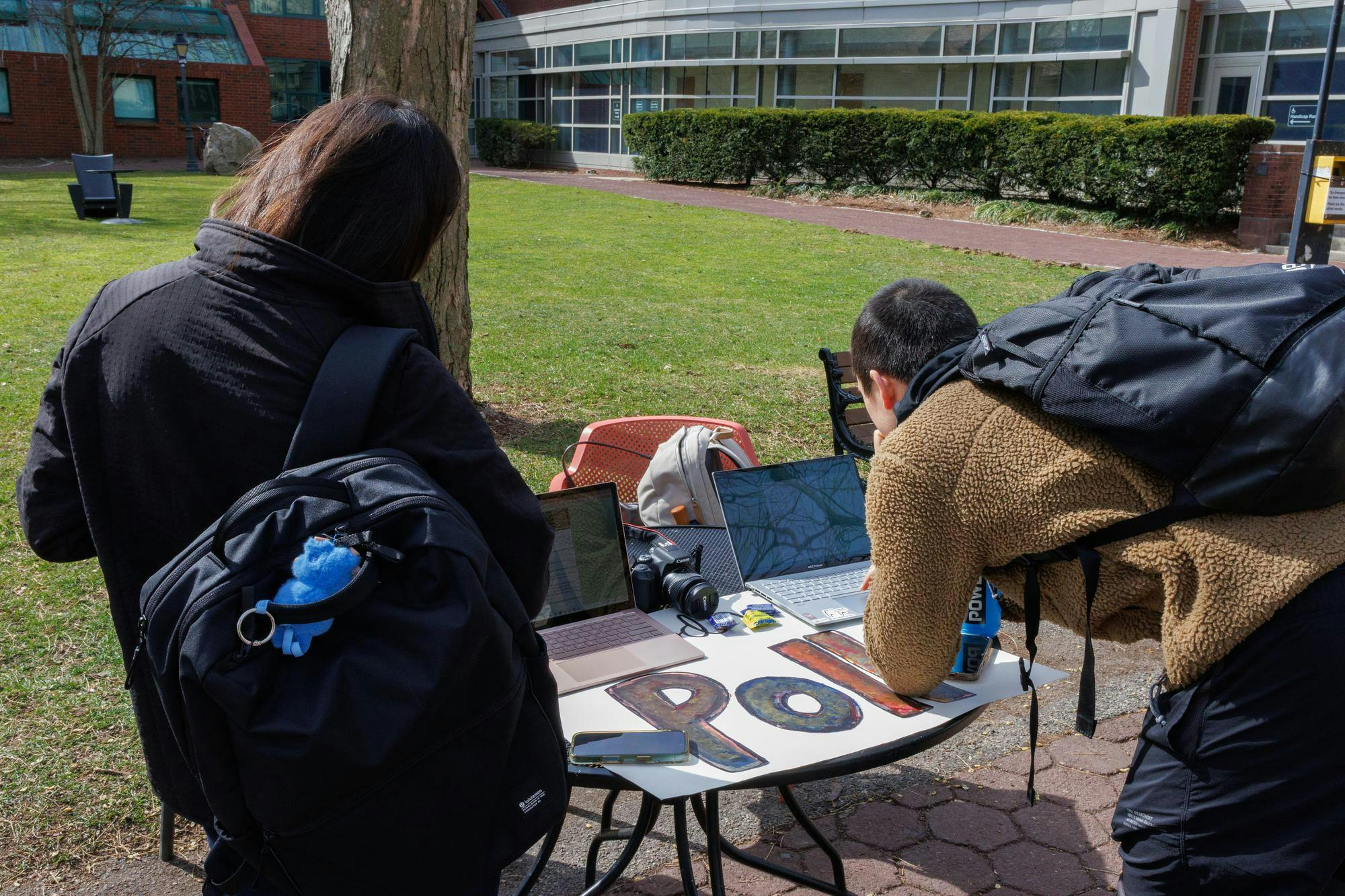 Two students lean over a table and take the Herald’s poll on laptops.