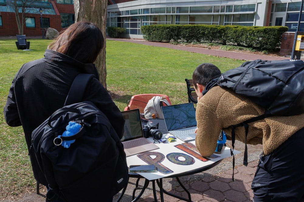 Two students lean over a table and take the Herald’s poll on laptops.