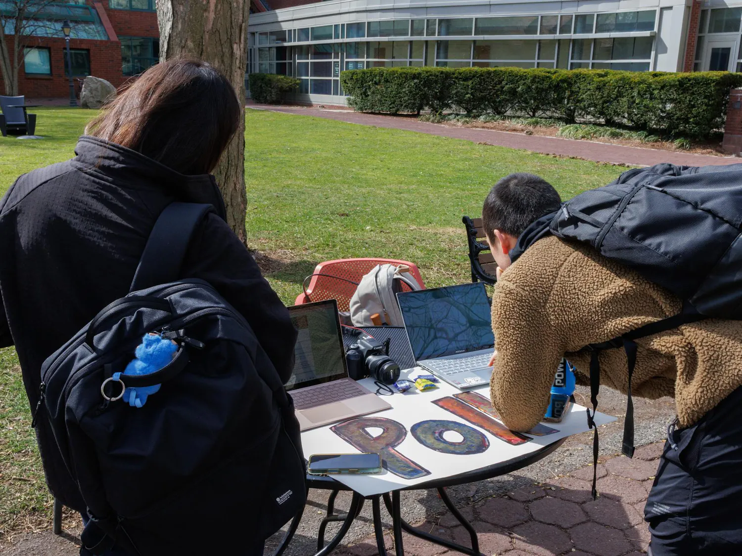 Two students lean over a table and take the Herald’s poll on laptops.