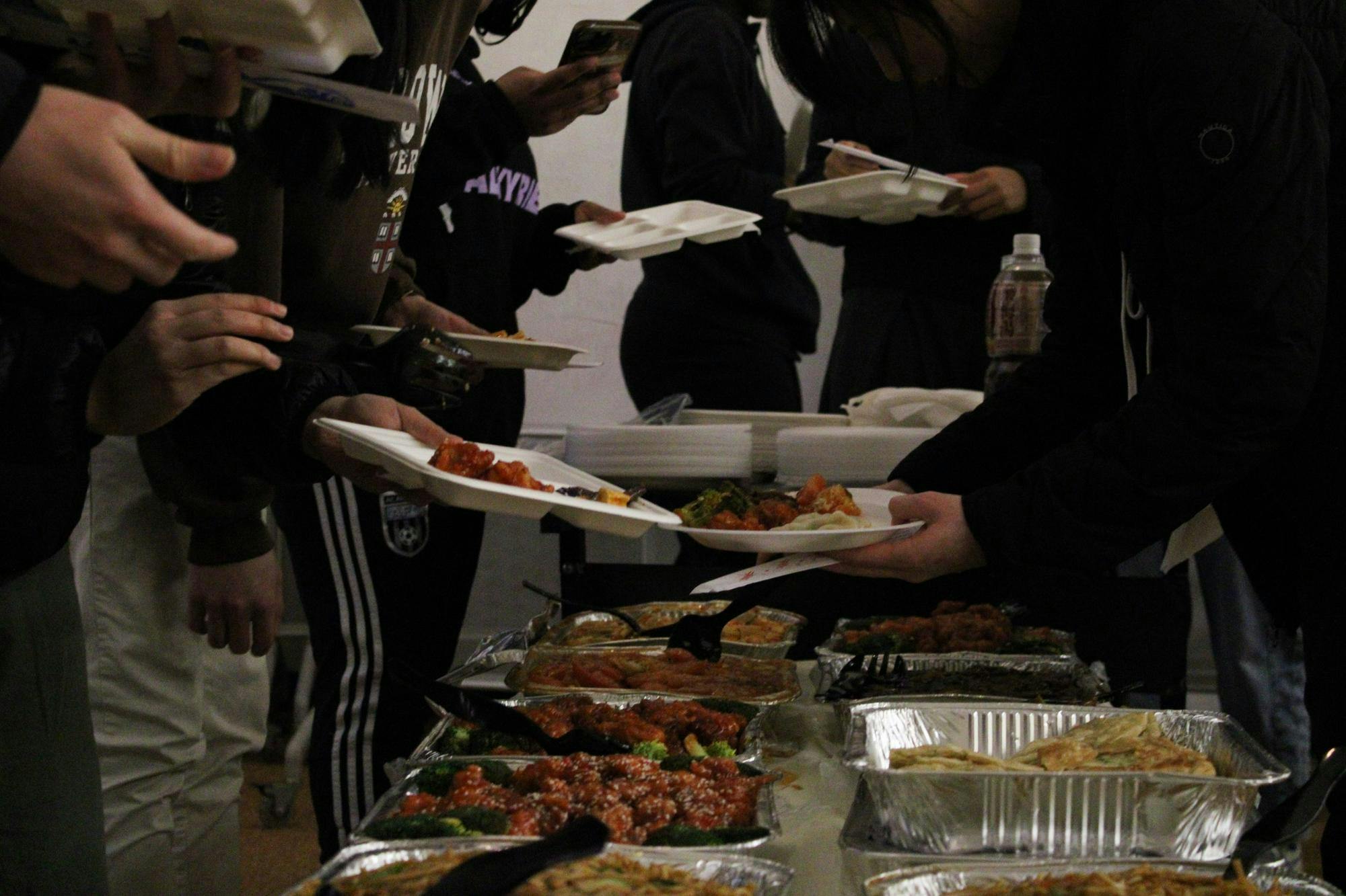 Photo of hands grabbing plates over aluminum dishes of different foods.

