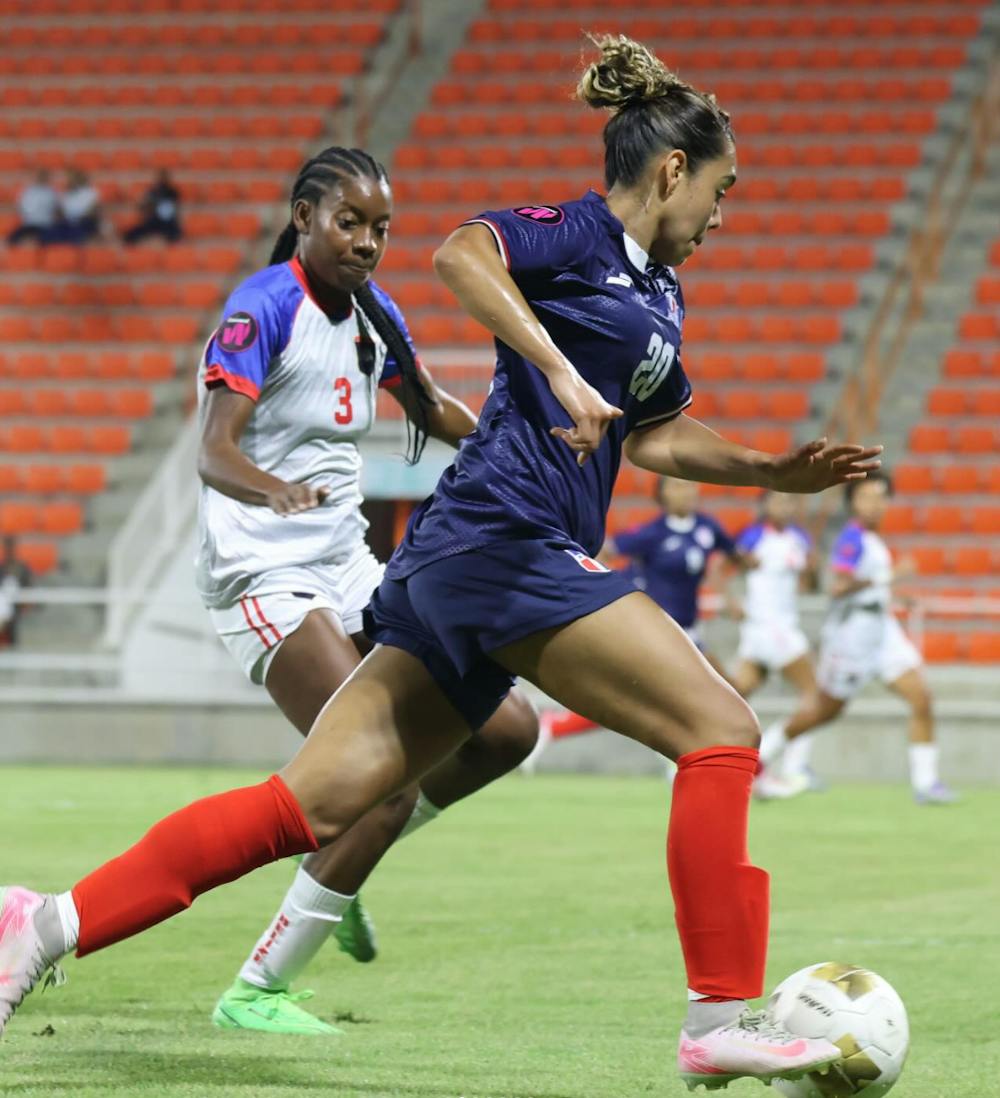 Angelina Vargas running on a football field while followed closely by another player.