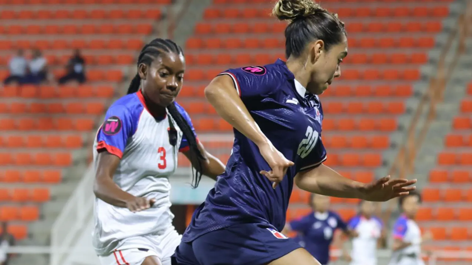 Angelina Vargas running on a football field while followed closely by another player.