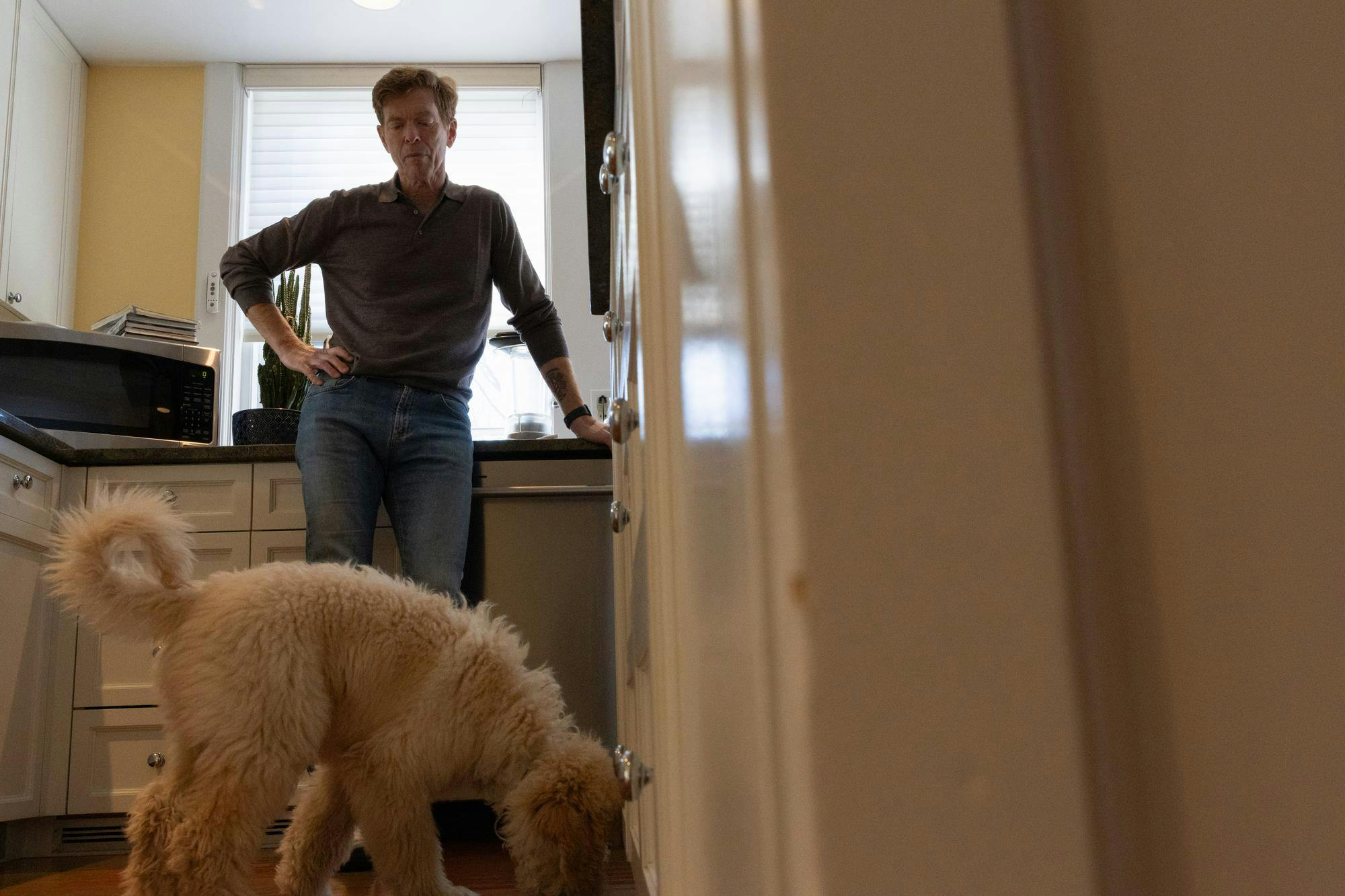 A man stands with his hand on his hip looking down at a dog.