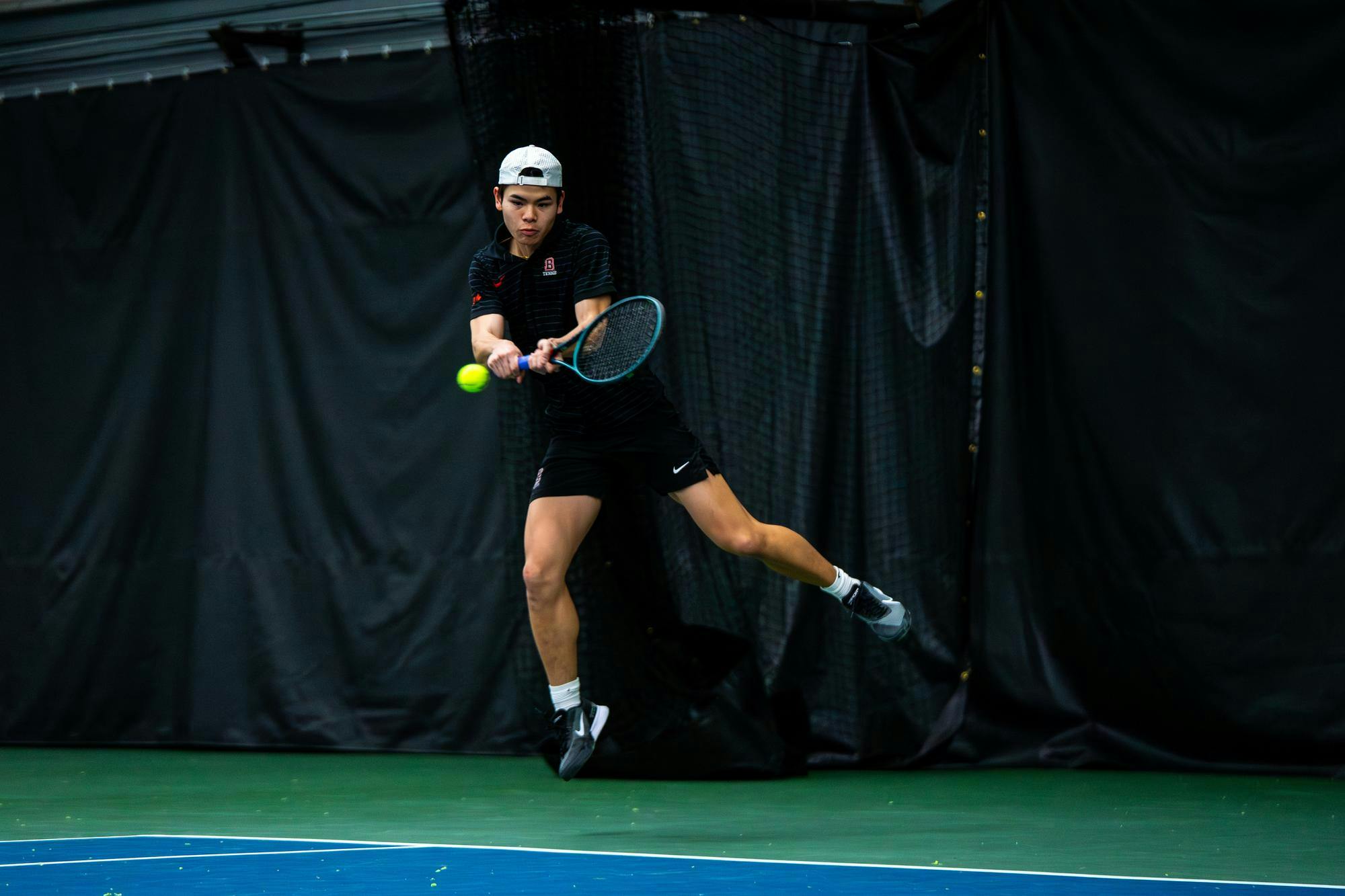 Action shot of a Brown tennis athlete swinging toward the ball. 
