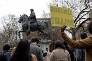 A photo of graduate students protesting in front of a statue of a man riding a horse. A yellow sign reads “RECOGNIZE FELLOWS.”
