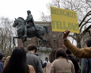 A photo of graduate students protesting in front of a statue of a man riding a horse. A yellow sign reads “RECOGNIZE FELLOWS.”