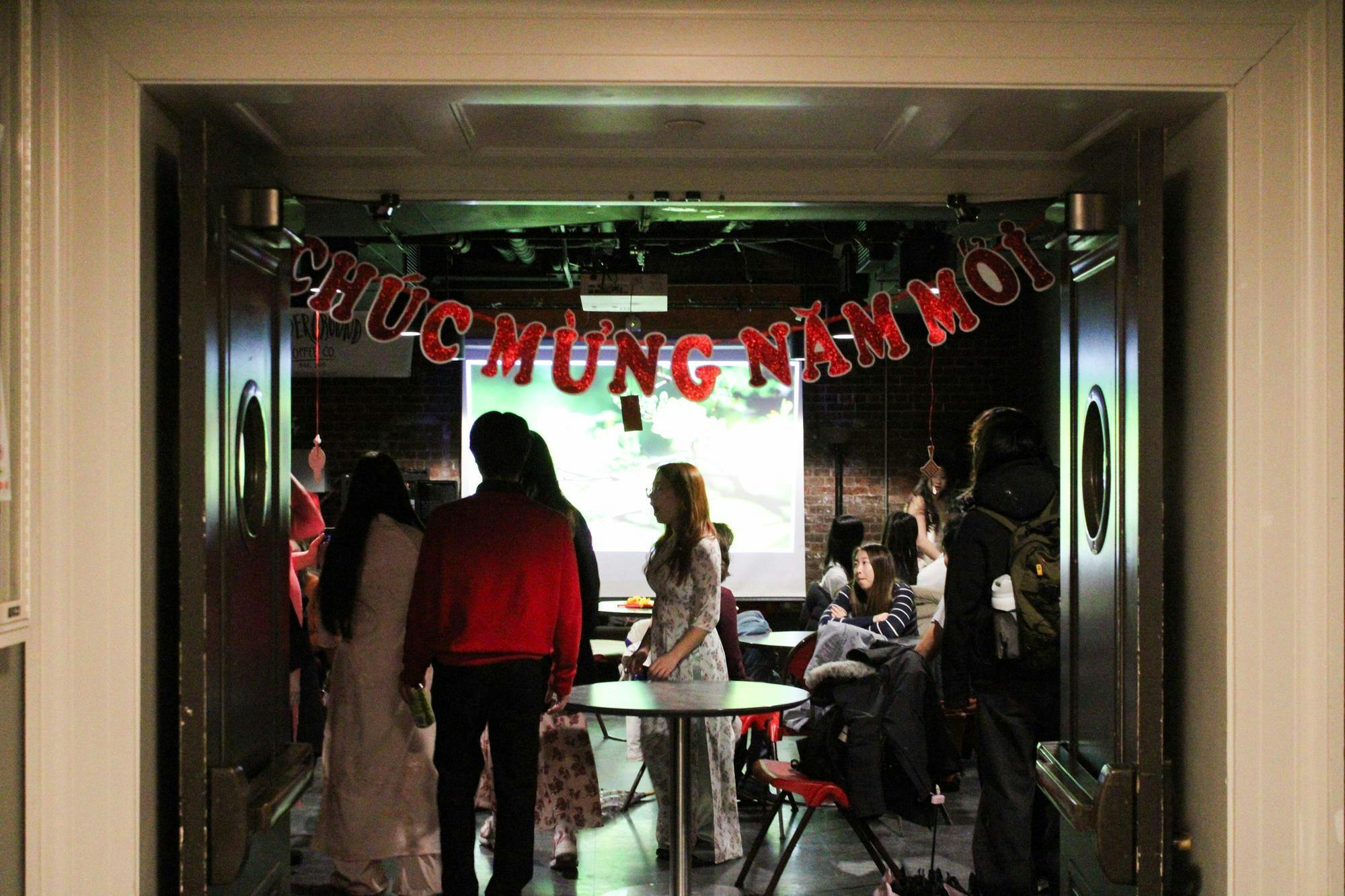 Photo of an open set of double doors with a string of red words saying “Chuc Mung Nam Moi” across the top with people inside.