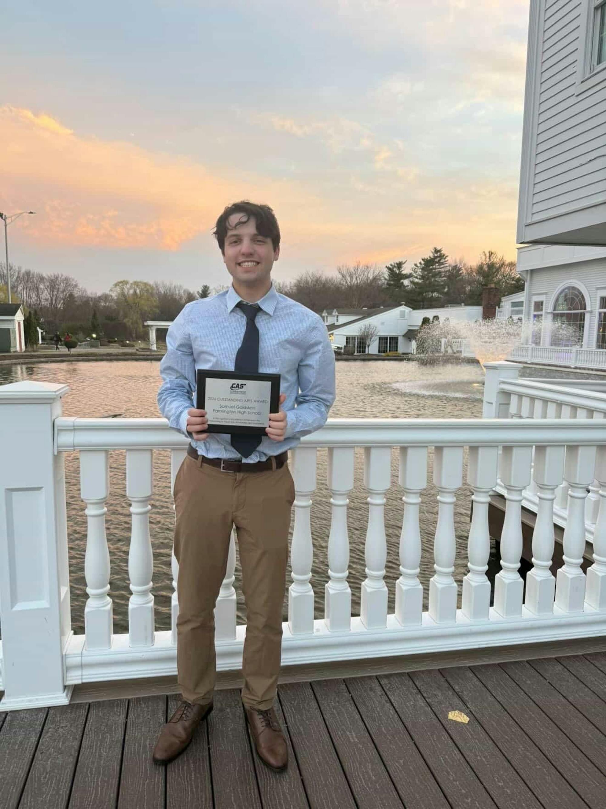 A photo of a boy holding a plaque in front of a sunset. 