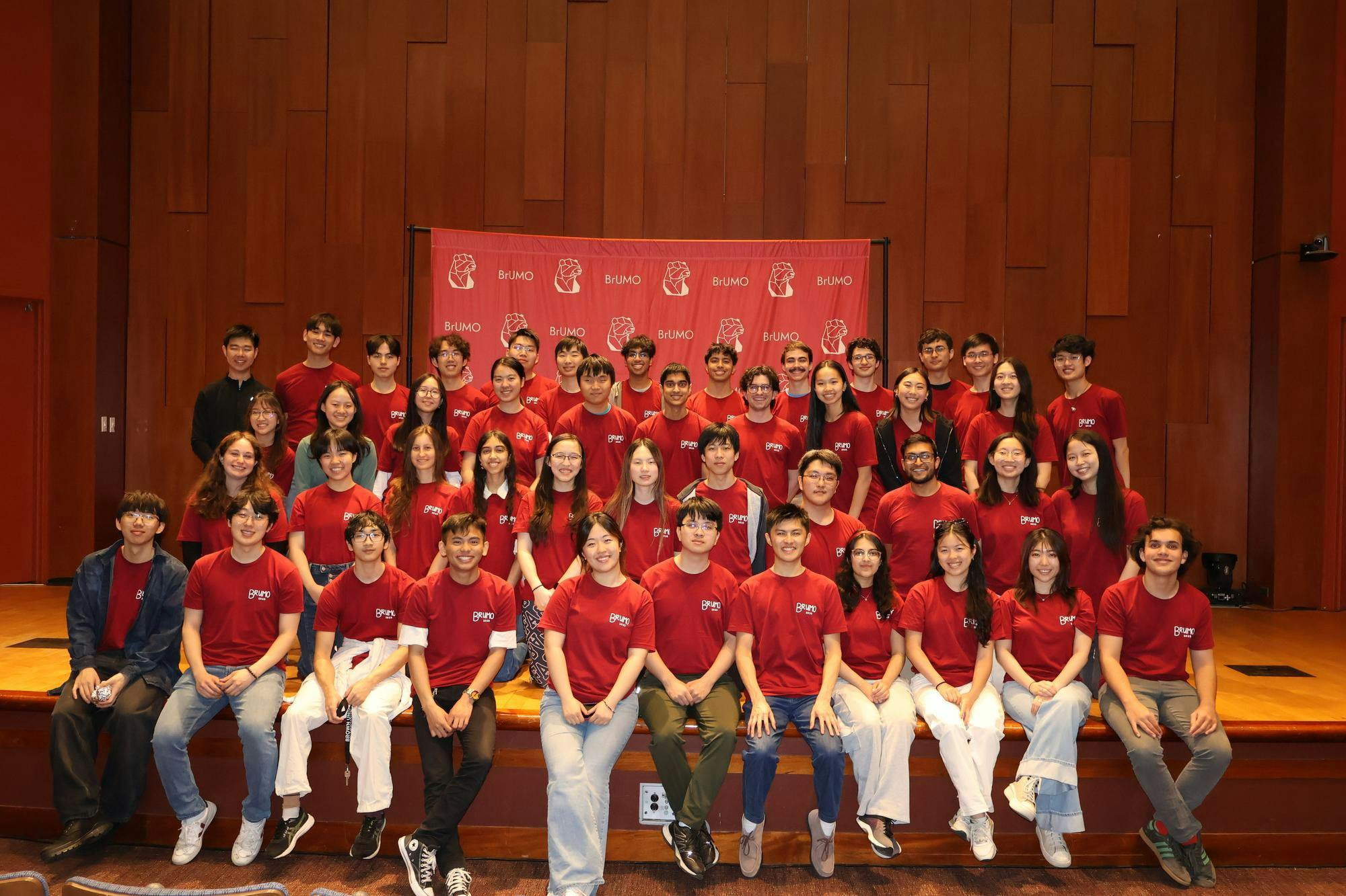 Team of 50 students wearing read shirts seated and standing in three rows in Salomon DECI. 