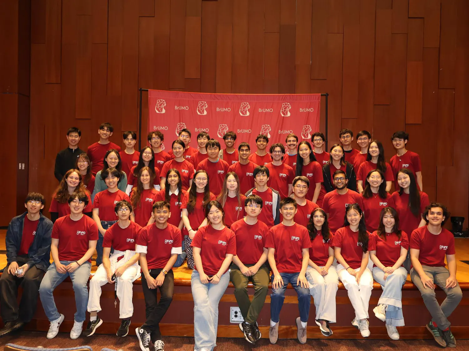 Team of 50 students wearing read shirts seated and standing in three rows in Salomon DECI.