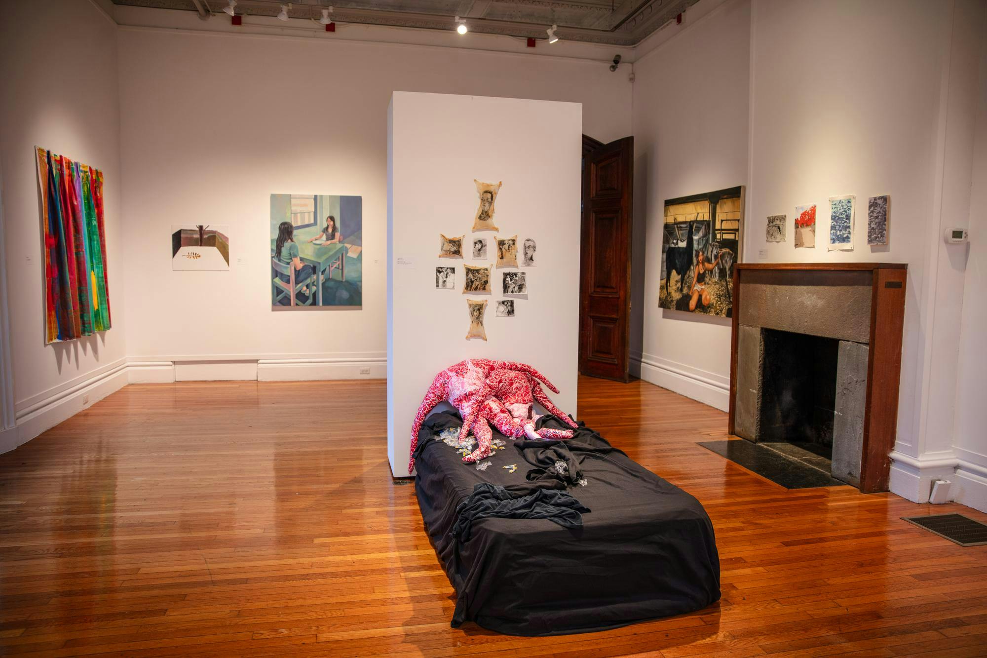 Photo of the exhibition on feature in RISD’s Woods-Gerry Gallery, featuring paintings, drawings, and a mattress-like piece with abstract figures atop it.